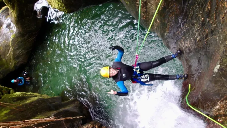 Canyoner giving thumbs up while abseiling above waterfall