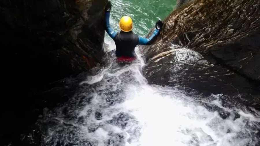 Canyoner sliding down natural water chute into canyon pool