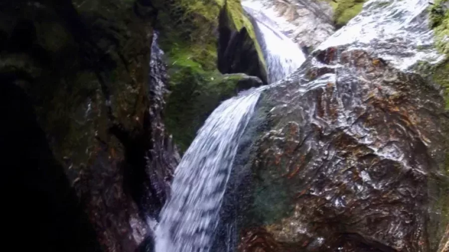 Tiered waterfall flowing through moss-covered canyon walls