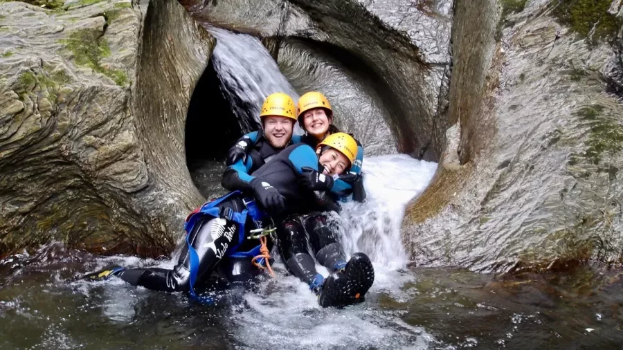 Three canyoners sliding together in natural water tunnel