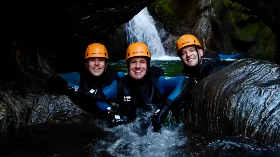 Three canyoners posing under rock arch with waterfall in background