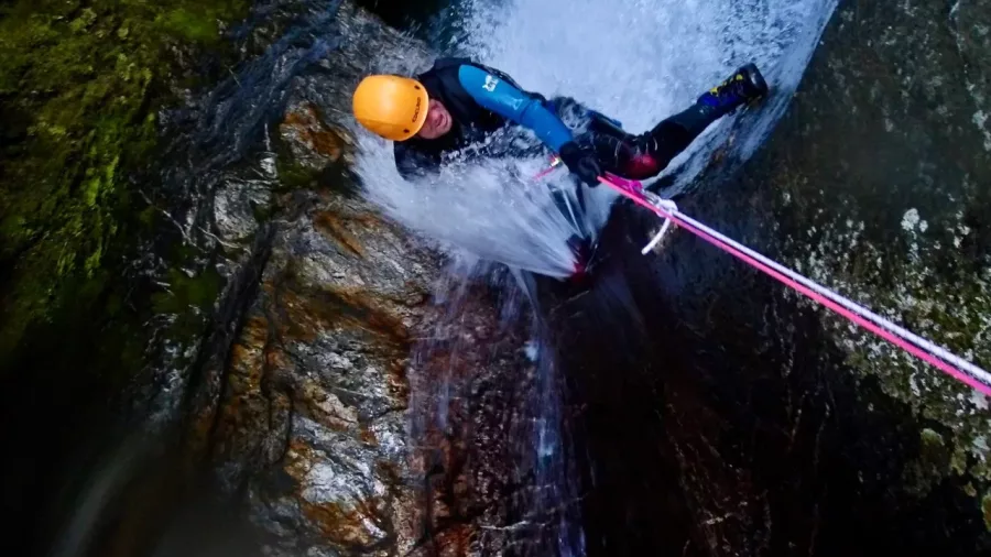 Canyoner descending steep wet rock face beside waterfall