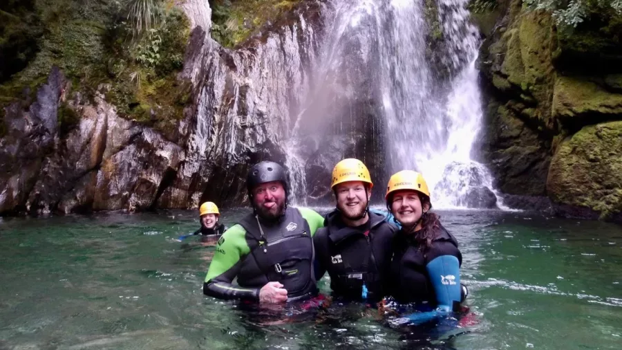 Group of canyoners smiling in water with waterfall behind