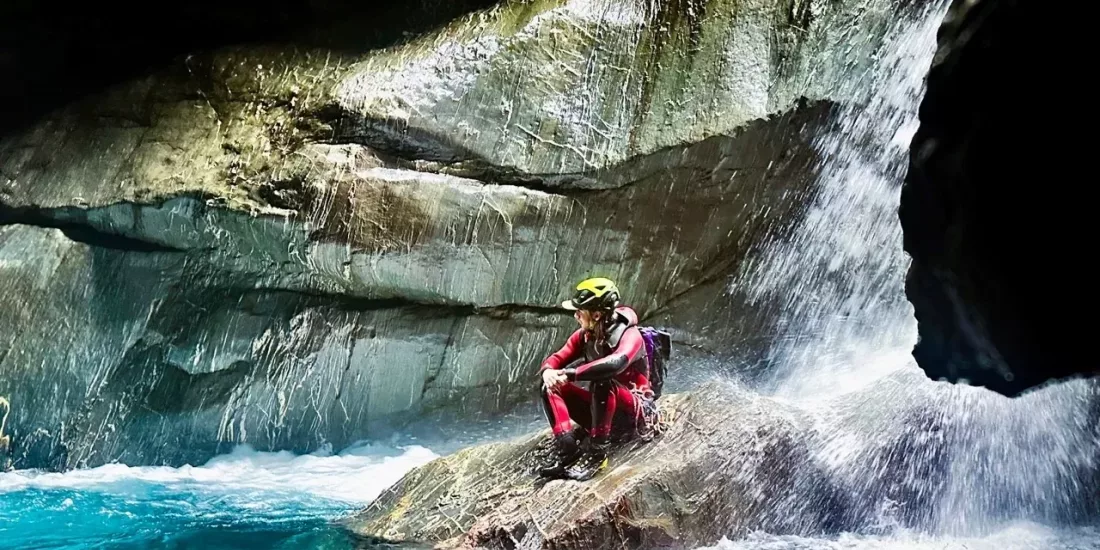 Canyoner sitting near waterfall edge inside canyon