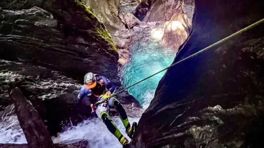 Canyoner rappelling down waterfall into turquoise pool