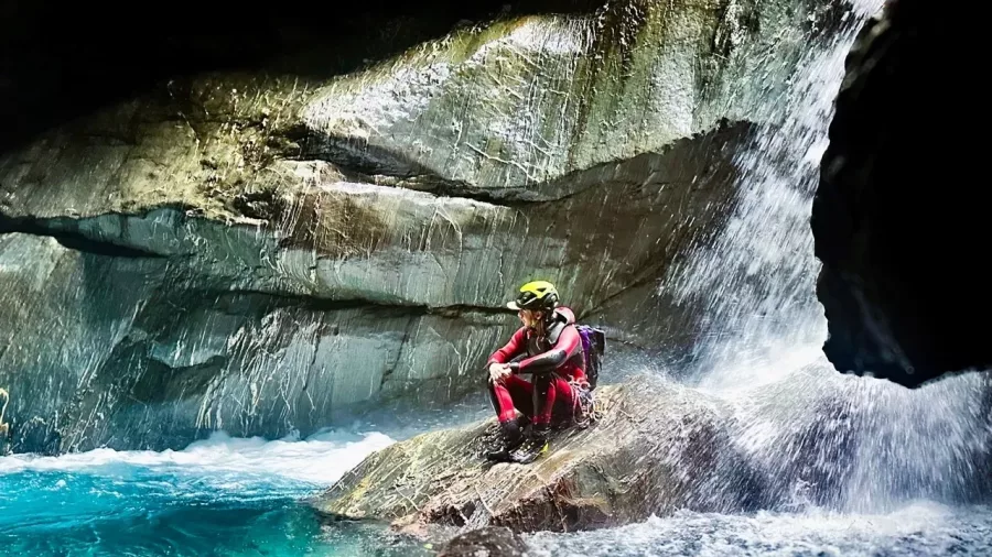 Canyoner sitting near waterfall edge inside canyon