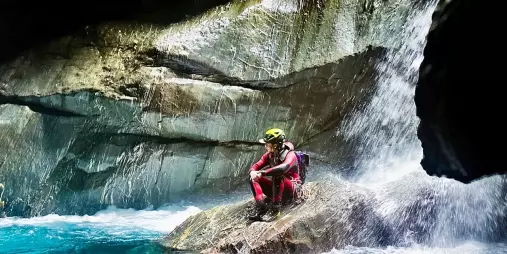 Canyoner sitting near waterfall edge inside canyon