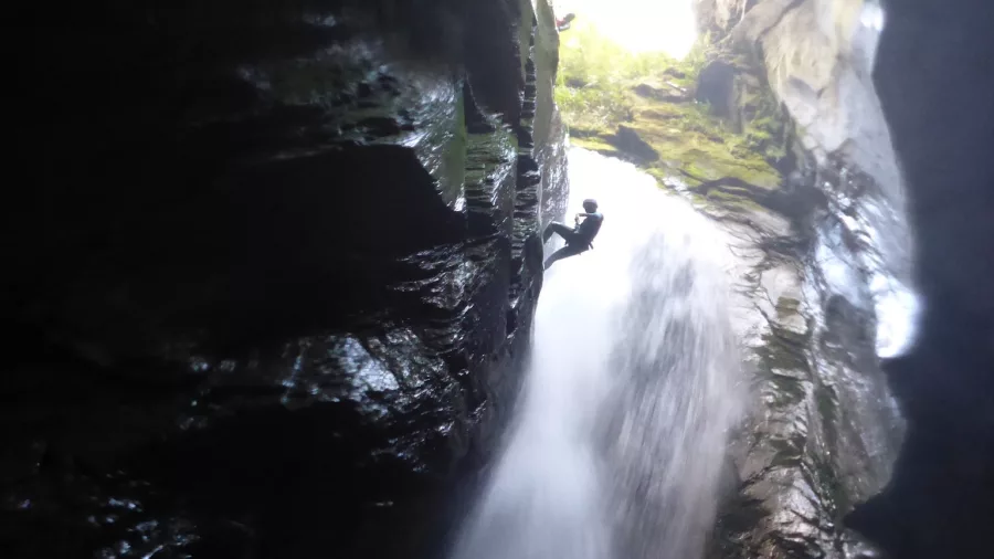 A silhouette of a canyoner mid-descent inside a cavernous canyon with light pouring from above.