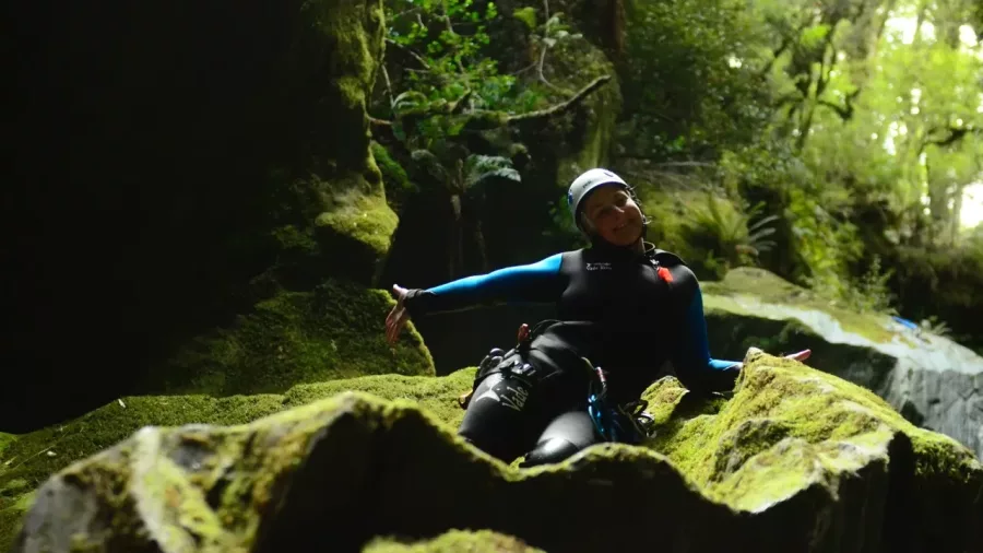 Canyoner resting on moss-covered rock in forest canyon