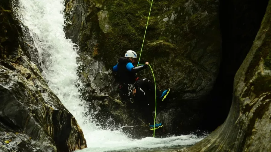 Canyoner descending rope beside roaring waterfall