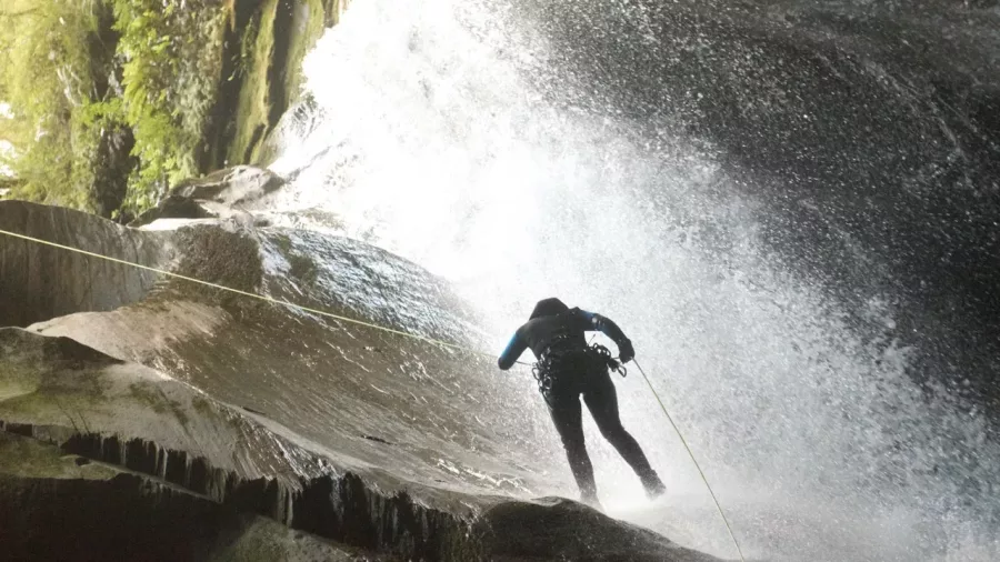 Canyoner descending in shadow beside roaring waterfall