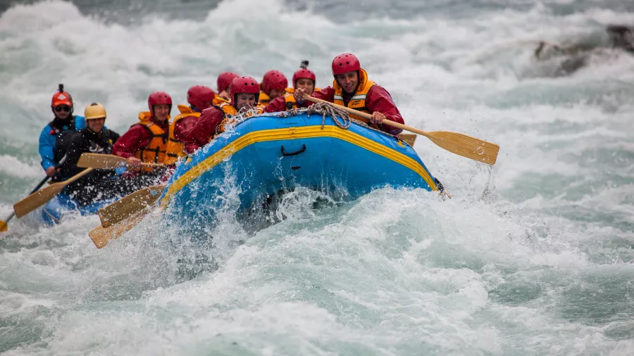 A group of rafters paddle through surging white water on the Kawarau River, led by a guide in a blue jacket.
