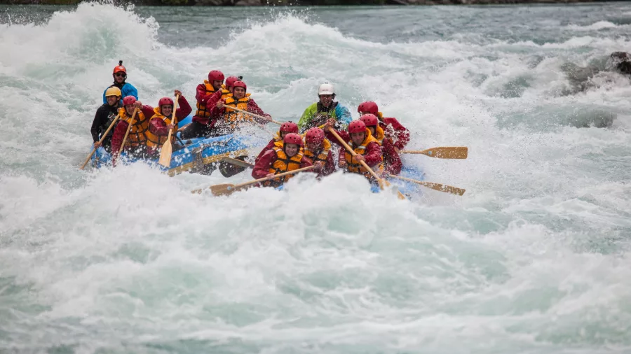 Two rafts tackle a big rapid simultaneously, creating waves and foam in every direction.