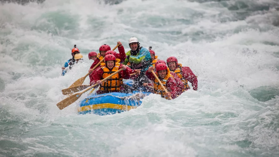 Rafters paddle hard through white water, with waves crashing over the raft’s front edge.