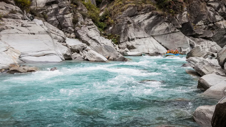 A raft navigates through narrow whitewater rapids in a rocky canyon on the Shotover River.