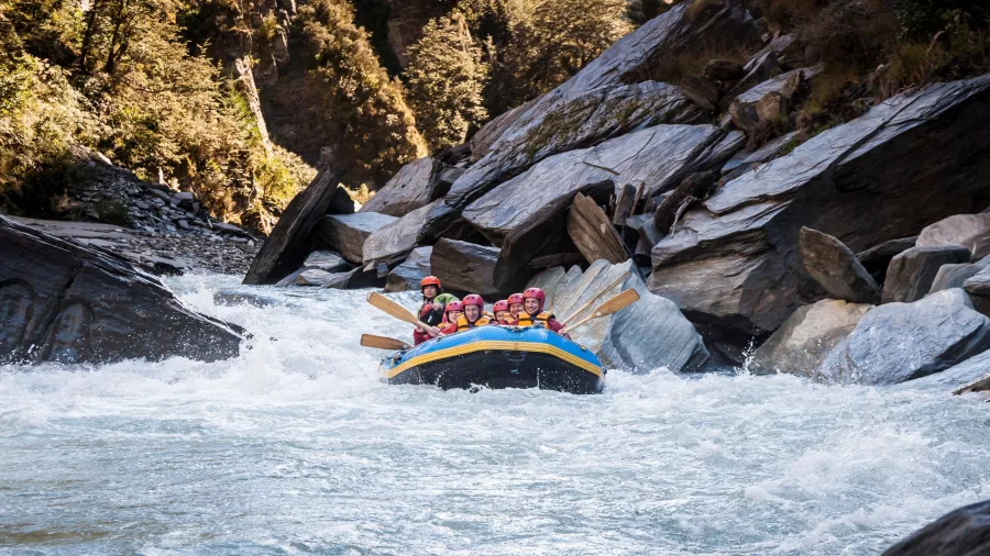 A blue raft surges through whitewater rapids between dark canyon walls on the Shotover River.