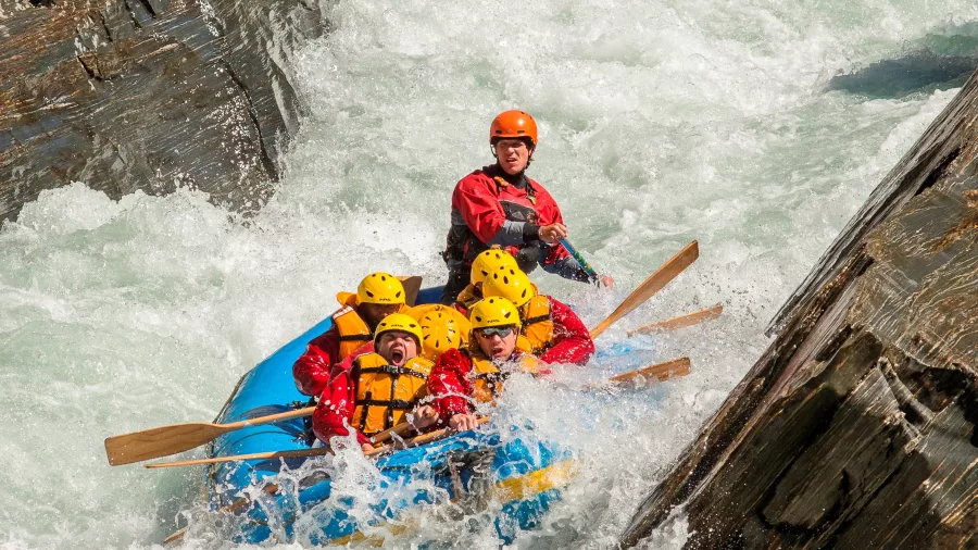 A rafting guide leads a group through swirling rapids between jagged canyon rocks.
