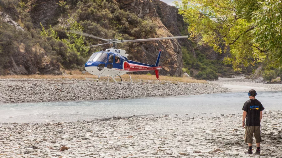 A helicopter hovers over a rocky riverbank, preparing for a post-rafting pickup.