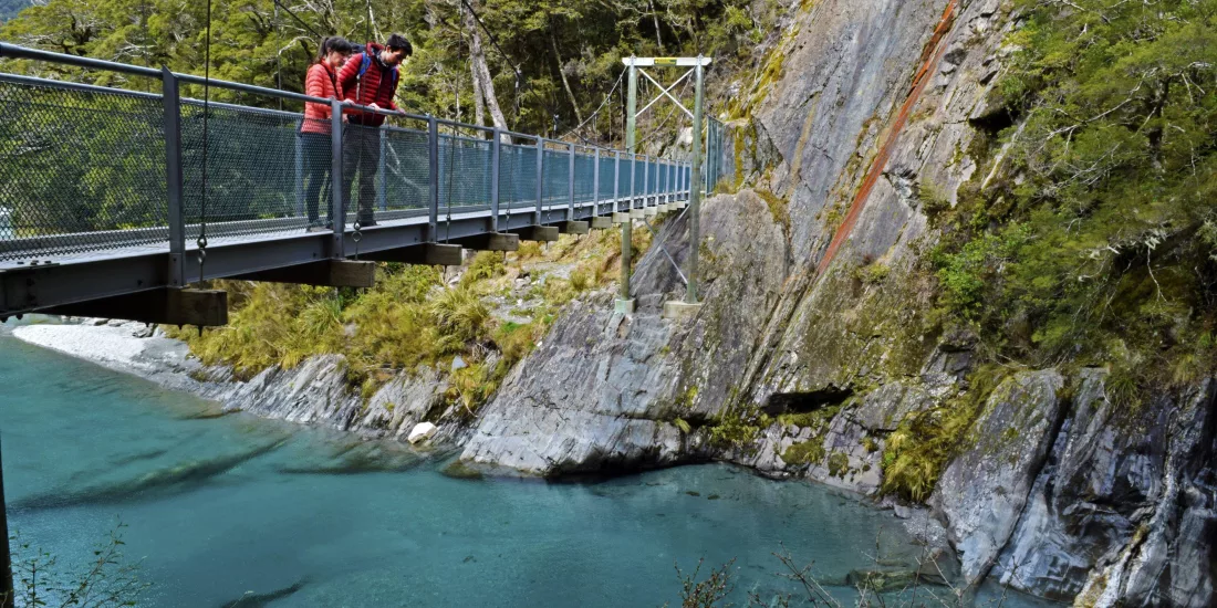 Tourists standing on swing bridge above Blue Pools in Haast