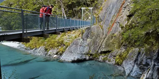 Tourists standing on swing bridge above Blue Pools in Haast