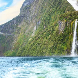 Tall waterfall cascading down a cliff into Milford Sound, seen from a boat