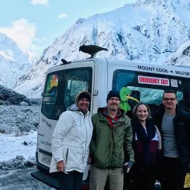 Group of travellers on a guided Milford Sound tour in winter, standing beside a scenic tour van in a snowy Fiordland landscape
