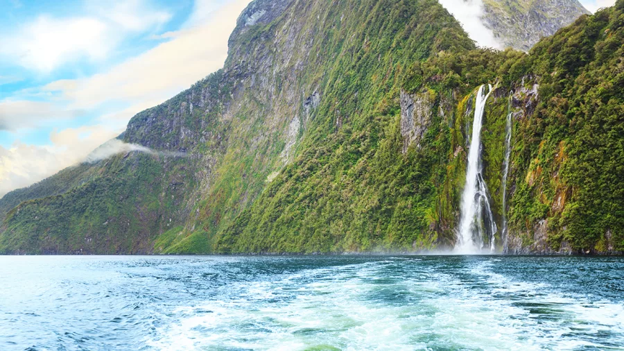 Tall waterfall cascading down a cliff into Milford Sound, seen from a boat