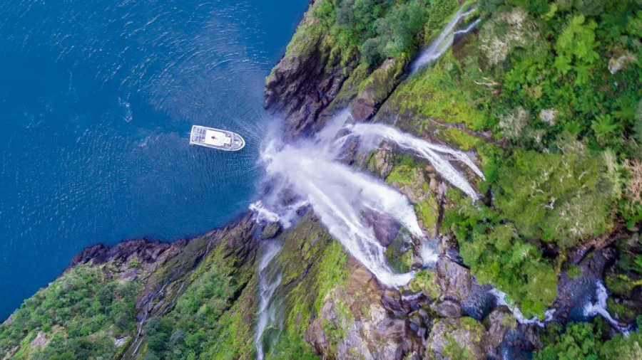 Aerial view of a cruise boat approaching a multi-stream waterfall in Milford Sound