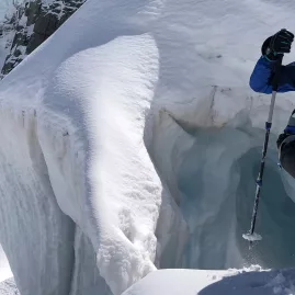 Smiling hiker with poles standing next to a glacier crevasse during a guided tour in Mount Cook National Park