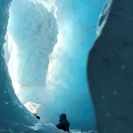 Person exploring a deep blue ice cave on the Tasman Glacier as part of a guided Mount Cook tour