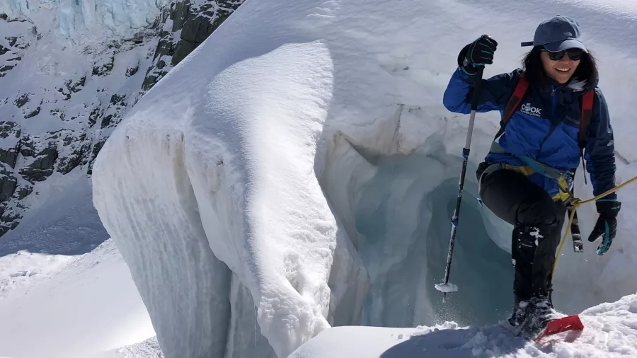 Smiling hiker with poles standing next to a glacier crevasse during a guided tour in Mount Cook National Park