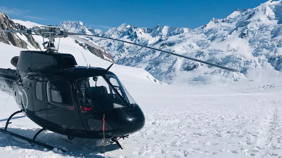 Black helicopter on a snow-covered landing site with Mount Cook and the Southern Alps in the distance