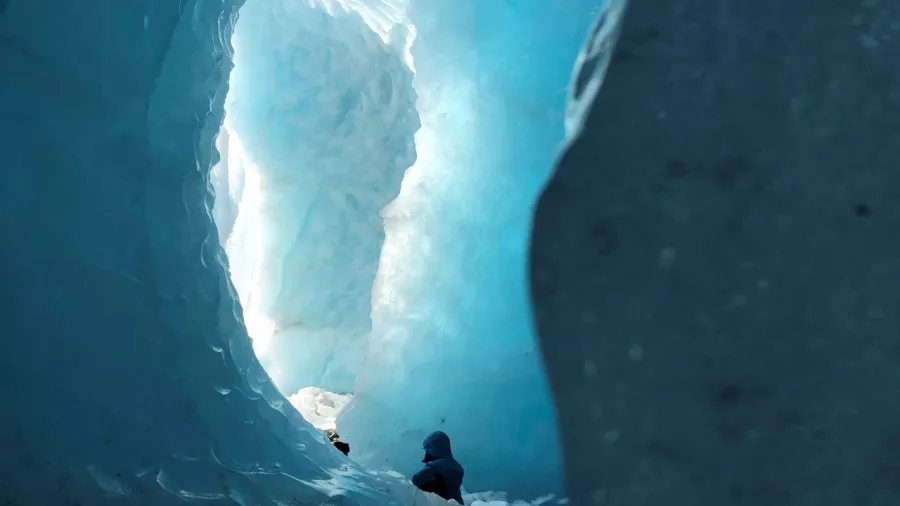Person exploring a deep blue ice cave on the Tasman Glacier as part of a guided Mount Cook tour