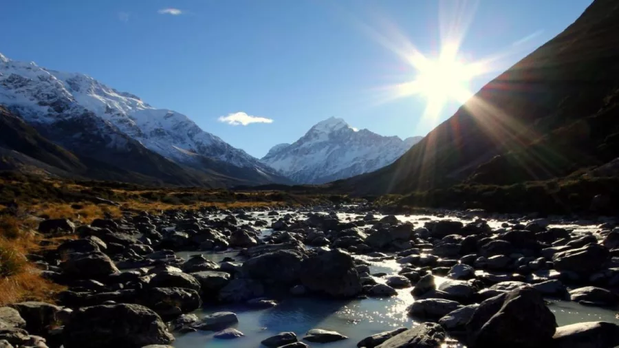 Sun shining over snow-capped peaks and rocky riverbed along the Hooker Valley Track in Mount Cook National Park