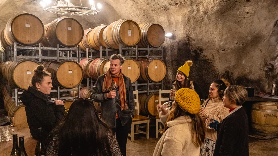 Group of visitors on a guided wine tasting inside Gibbston Valley’s famous wine cave, surrounded by oak barrels.
