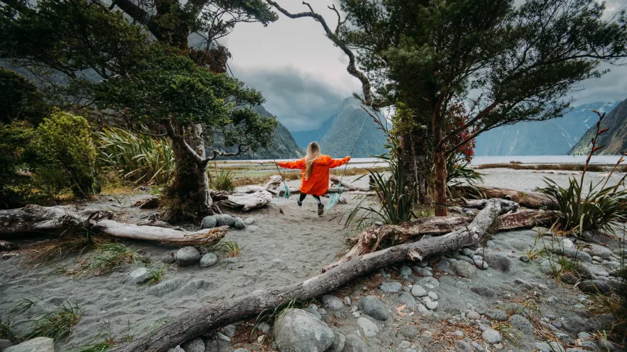 Person in red jacket enjoying the swing on Milford Sound’s foreshore with Mitre Peak in the background