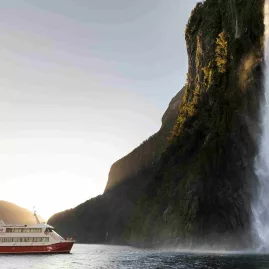 Milford Sound cruise boat sailing past Stirling Falls during sunset.