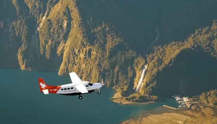 Light aircraft flying above Milford Sound with the marina, airstrip and Stirling Falls visible below in Fiordland National Park