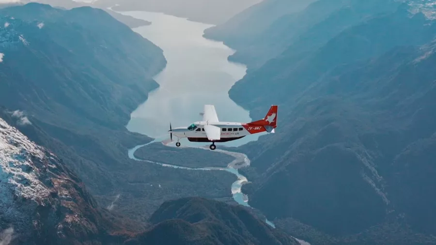 Glenorchy Air plane flying over Fiordland National Park with river and lake views below.