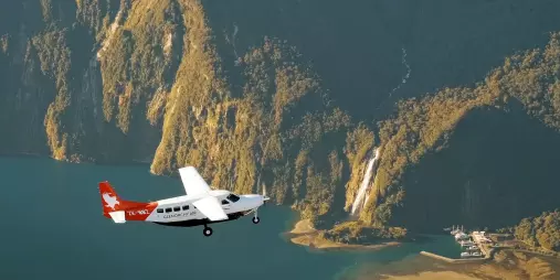 Light aircraft flying above Milford Sound with the marina, airstrip and Stirling Falls visible below in Fiordland National Park