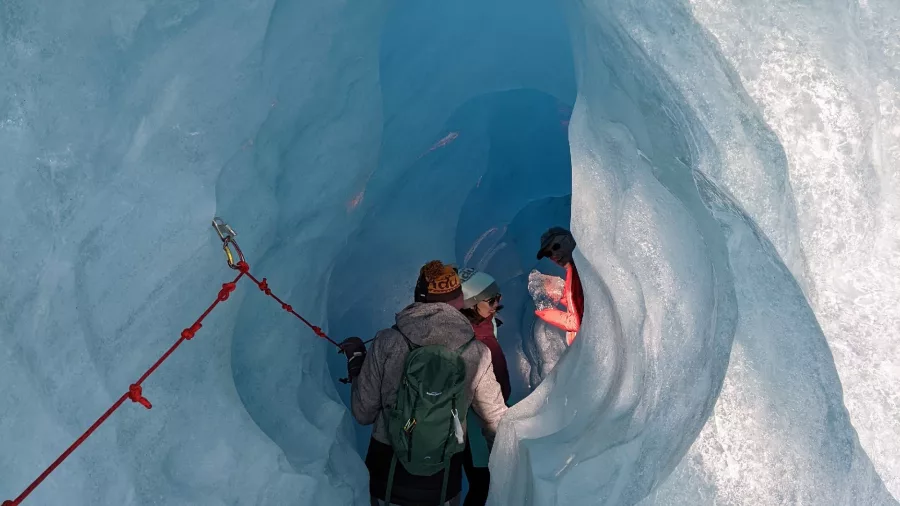 Glacier hikers exploring inside a vivid blue ice cave with safety rope