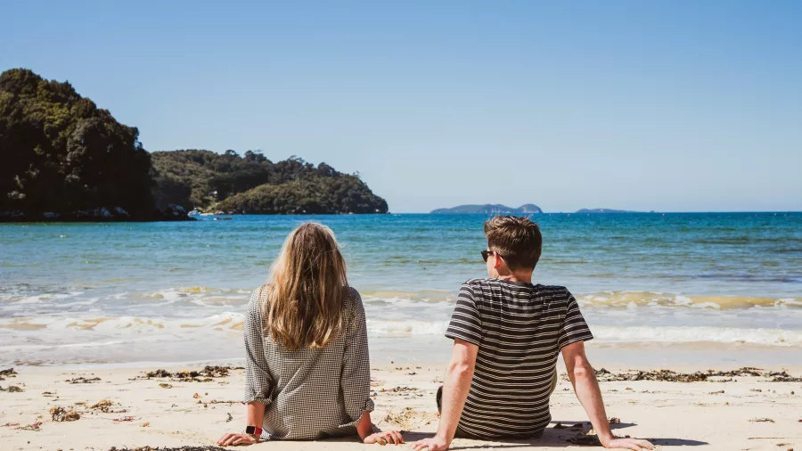 Couple sitting on Bathers Beach looking out over the ocean on Stewart Island