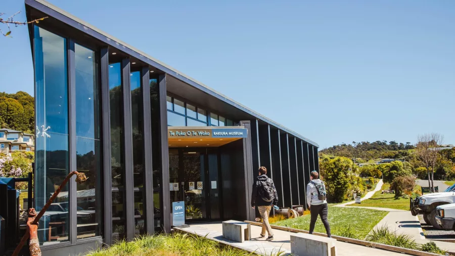 Two visitors approaching the modern glass entrance of Rakiura Museum in Oban, Stewart Island