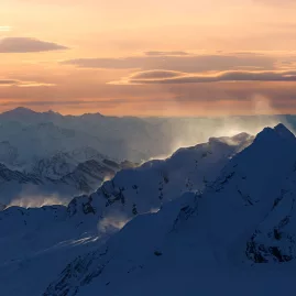 Southern Alps peaks lit by golden sunrise, with wind-whipped snow