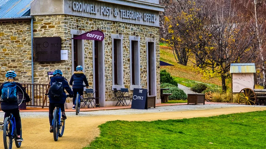 Cyclists riding past the historic Cromwell Post & Telegraph Office on the Lake Dunstan Trail