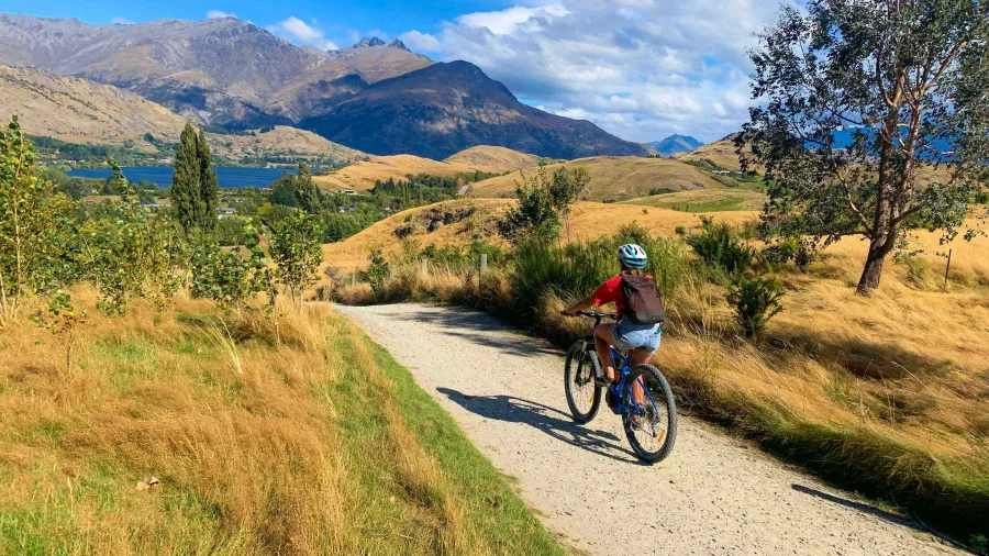 Cyclist on a gravel path overlooking Lake Wakatipu on the way to Gibbston Valley