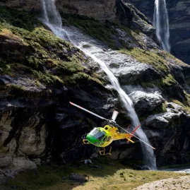 Yellow helicopter flying close to waterfalls at Earnslaw Burn