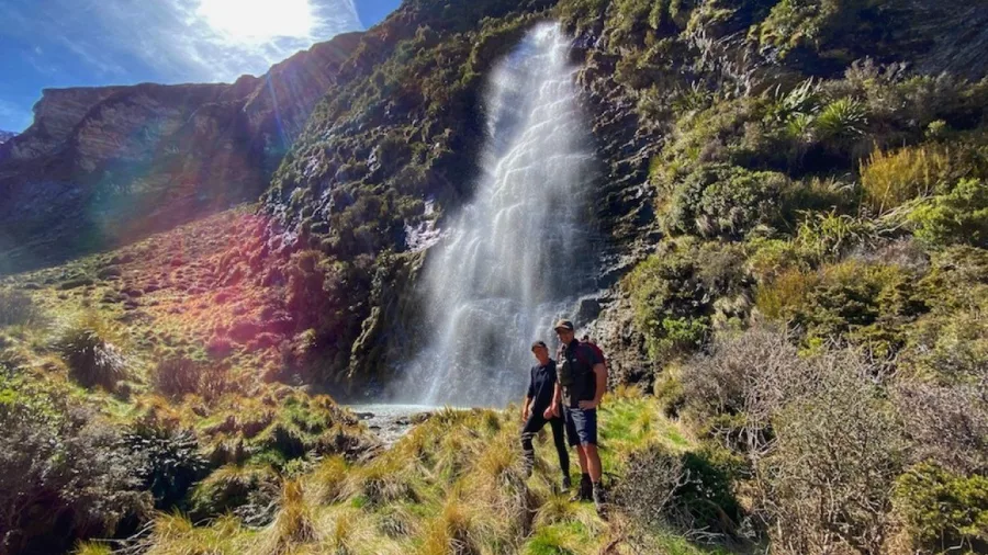Two hikers beside a waterfall on the Earnslaw Burn Heli Hike