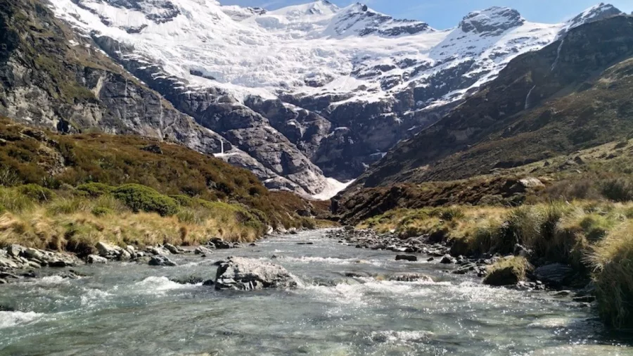 Clear glacial river flowing through Earnslaw Burn valley below snow-capped peaks