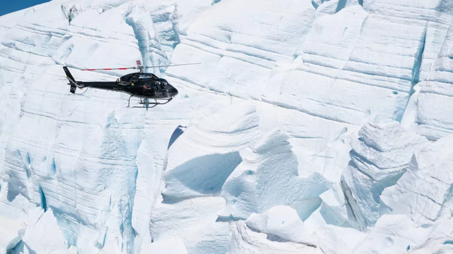 Helicopter flying low over dramatic blue glacier crevasses in New Zealand’s Southern Alps